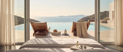 Blick aus einem Schlafzimmer auf Pool und Meerlandschaft mit heller Bettdecke im Vordergrund – Symbol für erholsamen Schlaf und sommerliche Entspannung.
