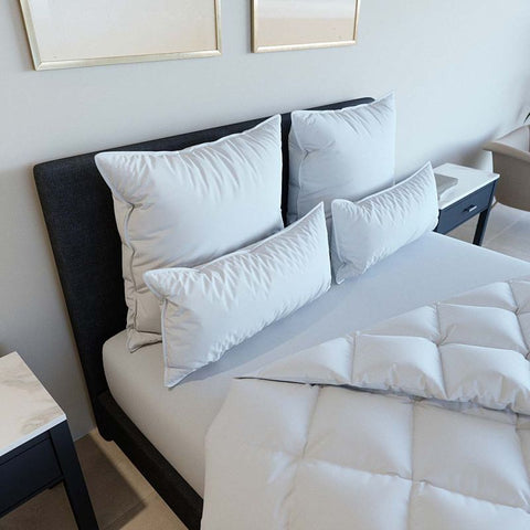 Modernes Bett mit mehreren weißen Kopfkissen und schmalen Kissen vor dunklem Kopfteil, arrangiert im Luxushotel-Stil für ein einladendes und komfortables Schlafzimmerambiente.