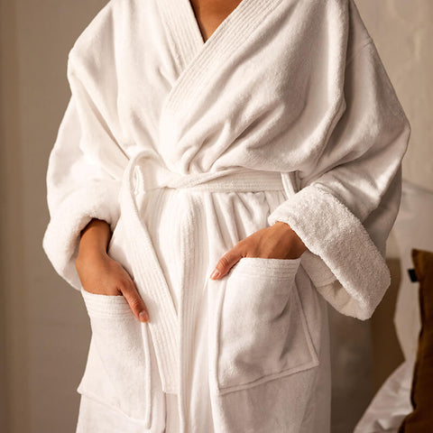 Person trägt einen weißen Bademantel aus weichem Frottee und vermittelt Komfort sowie das Ambiente eines luxuriösen Hotelaufenthalts.
