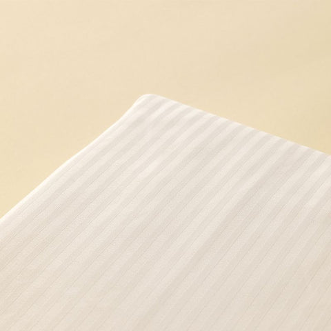 Detailaufnahme der Ecke eines Kissenbezugs aus weißer Microstripe Bettwäsche mit dezent glänzenden, eingewebten Längsstreifen vor einem warmen, beigen Hintergrund.