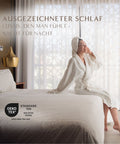 Frau im Bademantel genießt erholsamen Schlafkomfort mit OEKO-TEX zertifizierter Gänsedaunendecke im stilvollen Hotelzimmer