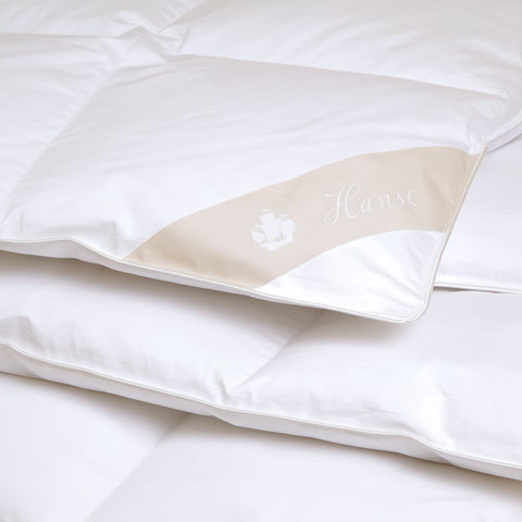 Detailaufnahme einer hochwertigen weißen Daunendecke mit feiner Verarbeitung und weichem Baumwollbezug in Hotelqualität.