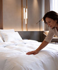 Qualitätsprüfung einer luxuriösen weißen Daunendecke am fertig bezogenen Bett für höchsten Schlafkomfort und Hotelqualität.