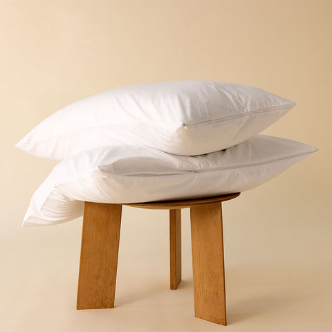 Zwei weiße Kissen mit hochwertigem Kissenschonbezug auf einem Holzhocker, sauber verarbeitet und elegant präsentiert.