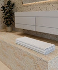 Premium Luxushotel Badematten 3er Set mit sauber gefalteten weißen Badematten auf einer Natursteinbank in einem modernen Badezimmer.